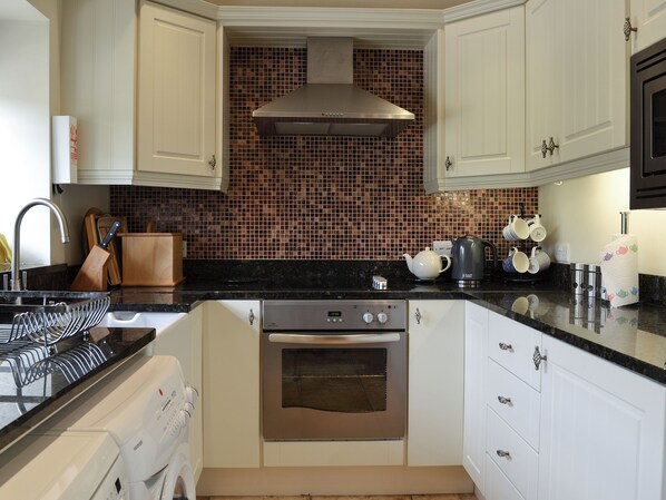 A kitchen with white cabinets, a stainless steel oven, a black countertop, and a tiled backsplash.