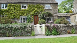 A stone house with a white picket fence, a wooden door, and a small garden with flowering plants. - 3 bedroom accommodation in Burnsall (Burnsall)