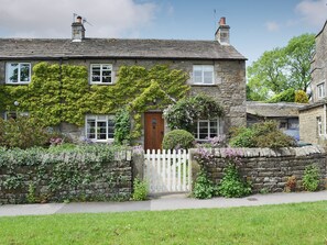 A stone house with a white picket fence, a wooden door, and a small garden with flowering plants.