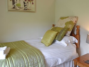 A neatly made bed with a green bedspread, two pillows, and a wooden headboard.