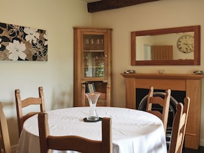 Comedor con una mesa redonda, sillas, una vitrina con puertas de vidrio, chimenea y un reloj de pared.
