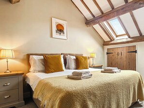 Un dormitorio con cama, dos mesitas de noche, un armario de madera, un tragaluz y un cuadro enmarcado en la pared.