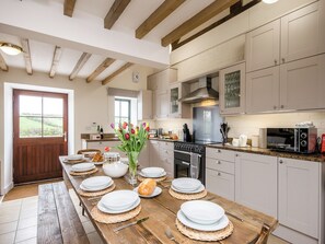 A kitchen with wooden beams, a stove, a microwave, and a view of the outdoors through a window.