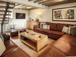 A living room with a brown leather sofa, wooden coffee table, and a TV mounted on the wall. - 7 bedroom accommodation in Bradbourne, near Ashbourne (Bradbourne, near Ashbourne)