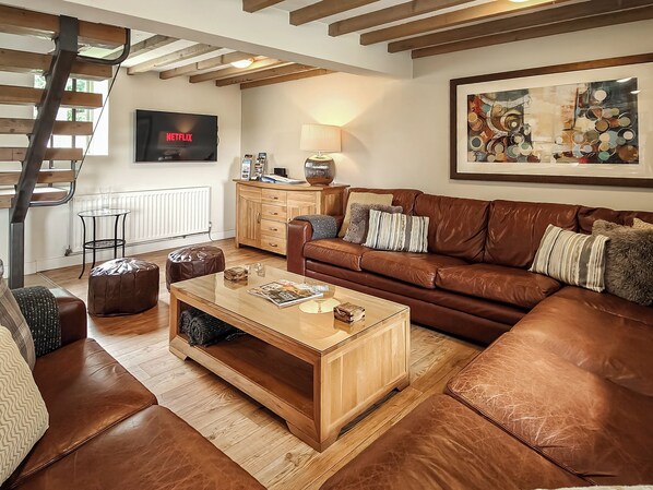 A living room with a brown leather sofa, wooden coffee table, and a TV mounted on the wall.