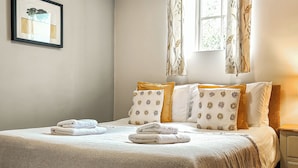 A neatly made bed with a white and beige bedspread, two pillows with floral patterns, and a window with curtains. - 7 bedroom accommodation in Bradbourne, near Ashbourne (Bradbourne, near Ashbourne)
