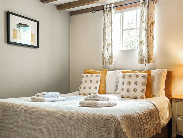 A neatly made bed with a white and beige bedspread, two pillows with floral patterns, and a window with curtains.