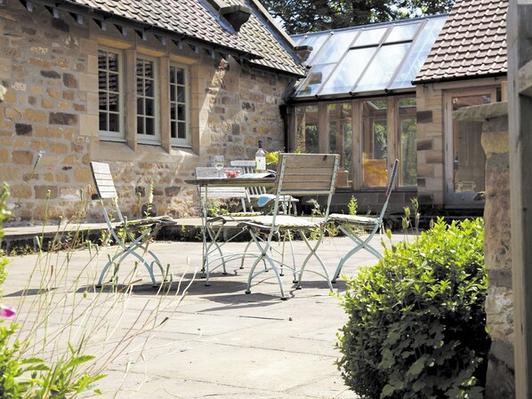 A stone building with a tiled roof, a glass-enclosed patio with a table and chairs, and a small garden area. - 3 bedroom accommodation in Thimbleby, near Osmotherley (Thimbleby, near Osmotherley)