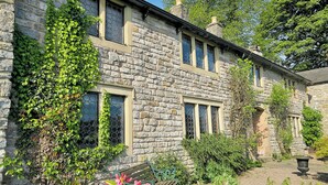 A stone building with multiple windows, a bench, and surrounding greenery. - 3 bedroom accommodation in Castleton (Castleton)