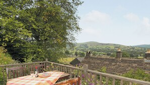 A wooden deck with a table and chairs, overlooking a rural landscape with houses and hills. - 3 bedroom accommodation in Castleton (Castleton)