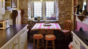 A rustic kitchen with a stone wall, wooden counter, and a table with a checkered tablecloth. - 3 bedroom accommodation in Castleton (Castleton)