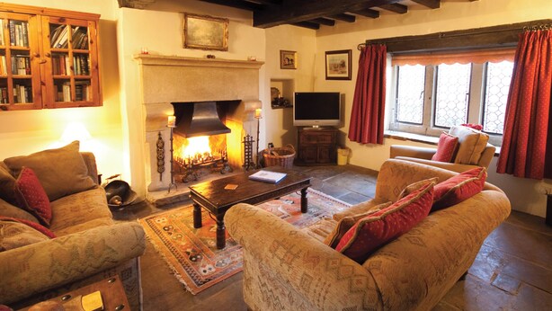 A cozy living room with a fireplace, wooden beams, a television, and comfortable seating. - 3 bedroom accommodation in Castleton (Castleton)