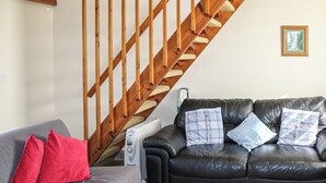 Un salon avec un canapé gris, un canapé en cuir noir agrémenté de coussins à motifs, un escalier en bois et un radiateur.
