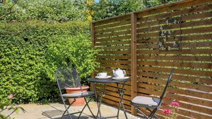 Une terrasse avec une table et des chaises, entourée d’une clôture en bois et d’une végétation luxuriante.
