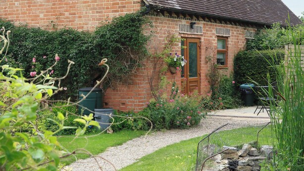 Une maison en briques avec un toit en pente, une porte d’entrée et un petit jardin avec un chemin de gravier menant à la porte.