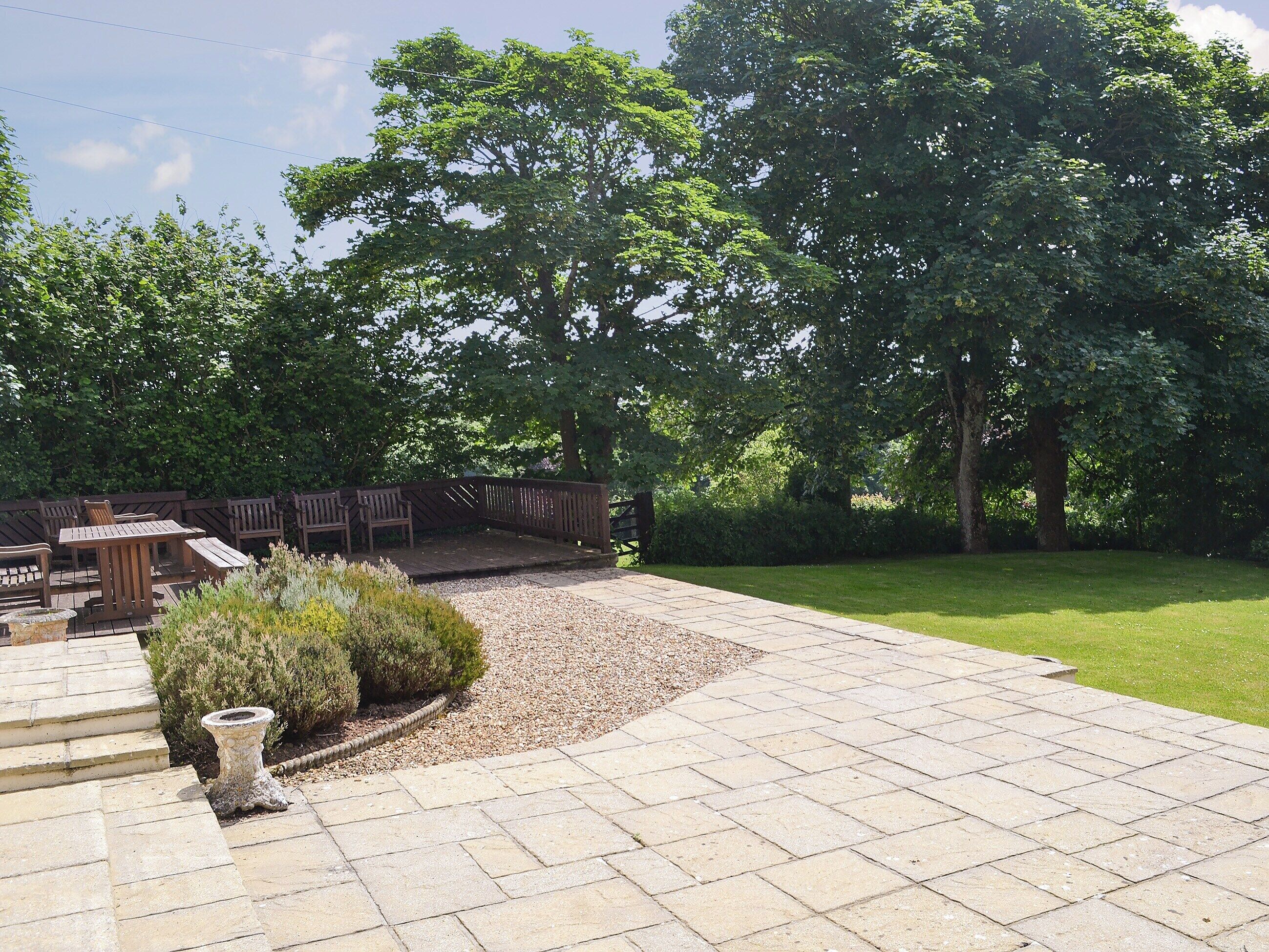 A patio with stone tiles, wooden furniture, and a small garden area with a bird bath.