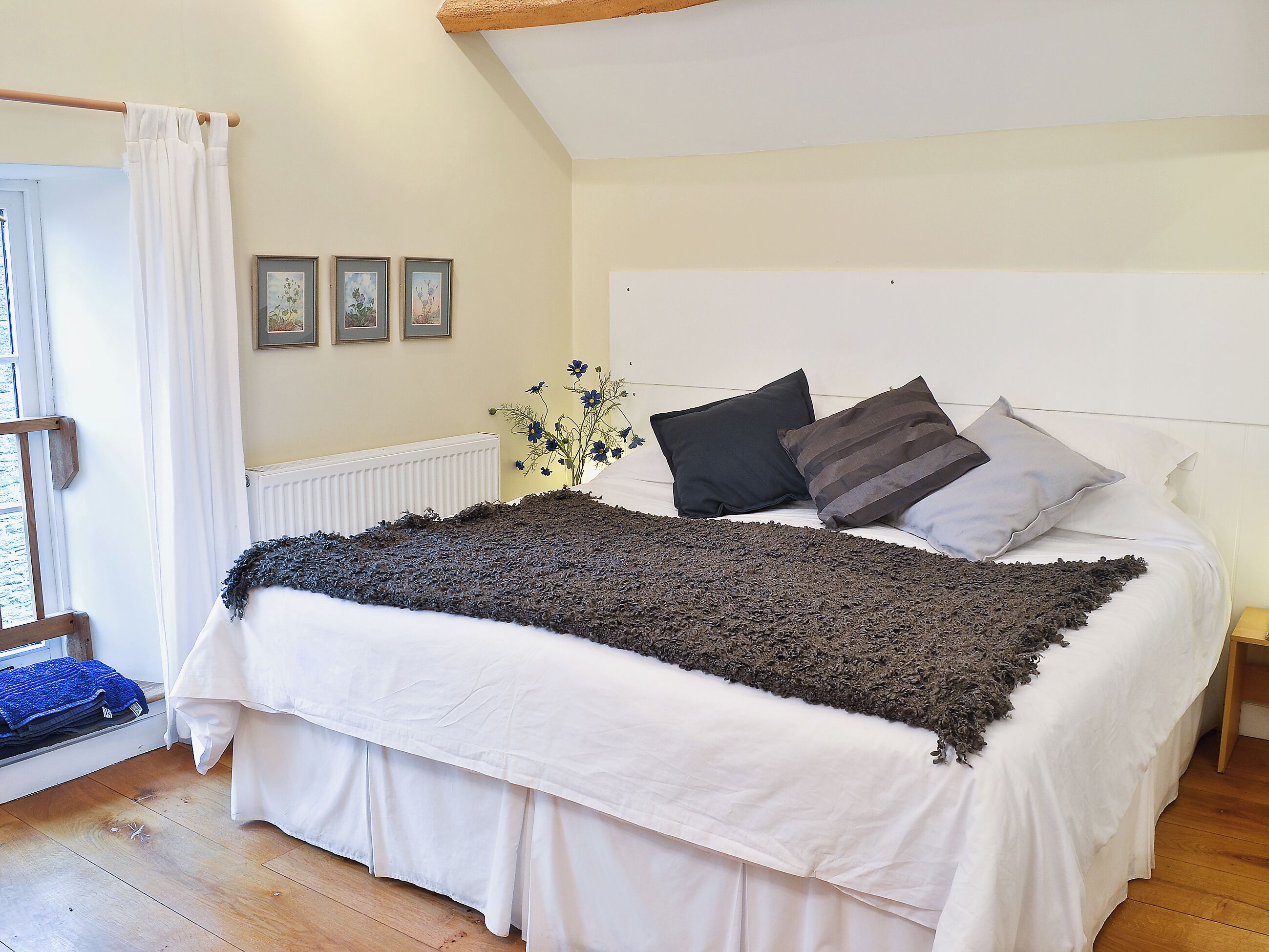 Een slaapkamer met een bed, een raam met gordijn, een radiator en een kleine plant.