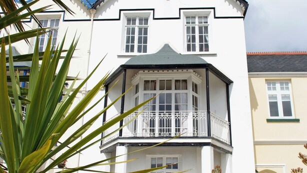 Een wit gebouw met een erker, een balkon met een witte balustrade en een rond raam boven de deur.