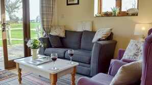 A living room with a grey sofa, a purple armchair, a white coffee table with two wine glasses, and a vase with flowers. - 2 bedroom accommodation in Hooe, Battle (Hooe, Battle)