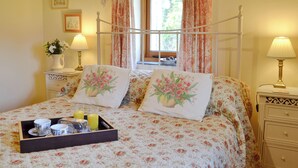 A bedroom with a four-poster bed, floral bedding, two bedside lamps, a window with curtains, a bedside table with a vase of flowers, and a tray with cups and a glass of orange juice. - 2 bedroom accommodation in Hooe, Battle (Hooe, Battle)
