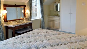 Un dormitori amb un llit, una tocador amb mirall, una finestra amb cortines i una porta.