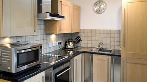 Een moderne keuken met roestvrijstalen apparatuur, houten kastjes en een zwart aanrechtblad, plus een wandklok.
