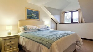 Een slaapkamer met een bed, nachtkastje, lamp, schilderij en een raam met gordijnen.