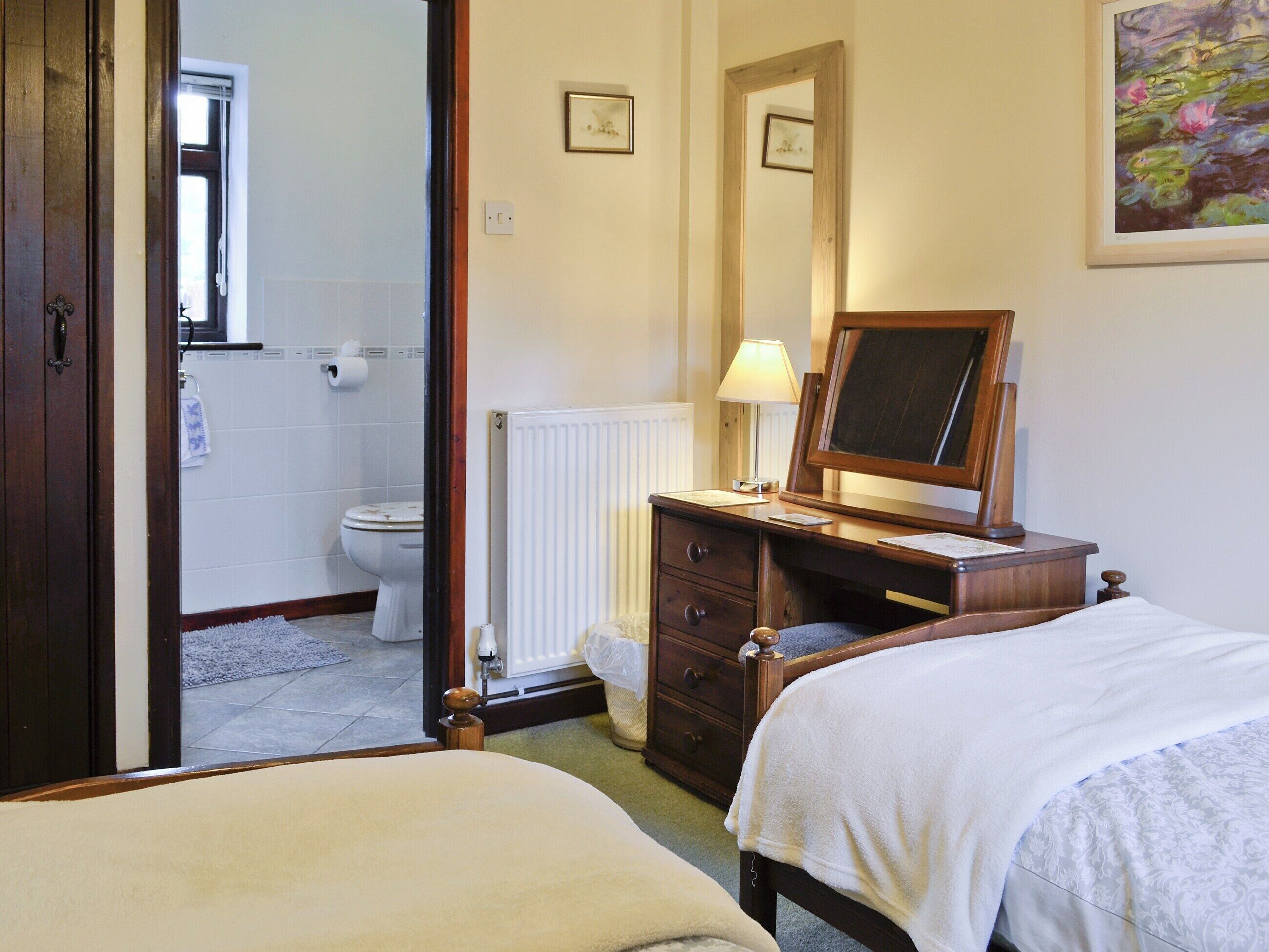 Une chambre d’hôtel avec un lit, une commode, un miroir, un radiateur et une salle de bain visible à travers une porte ouverte.