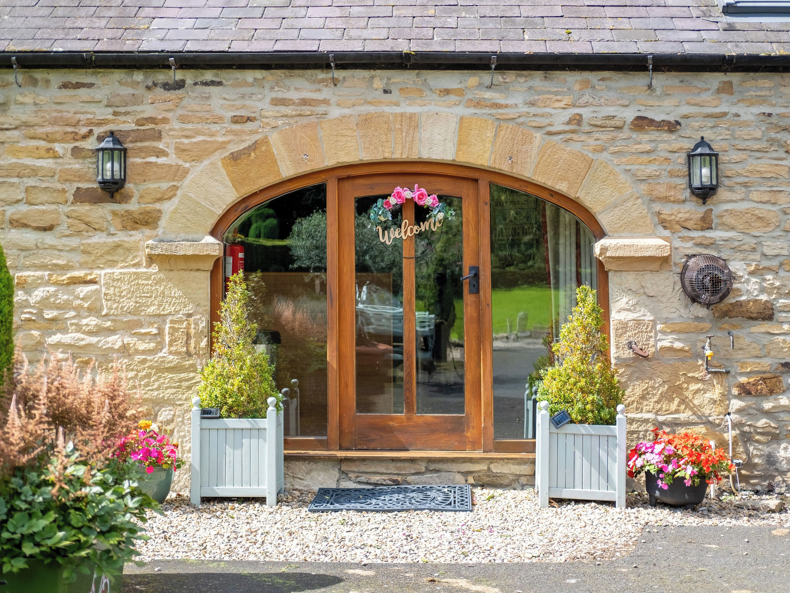 A stone building with a wooden entrance, a welcome sign, and two potted plants.