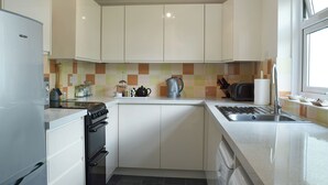Een compacte keuken met witte kasten, een inbouwoven, een vaatwasser en een raam voor natuurlijk licht.