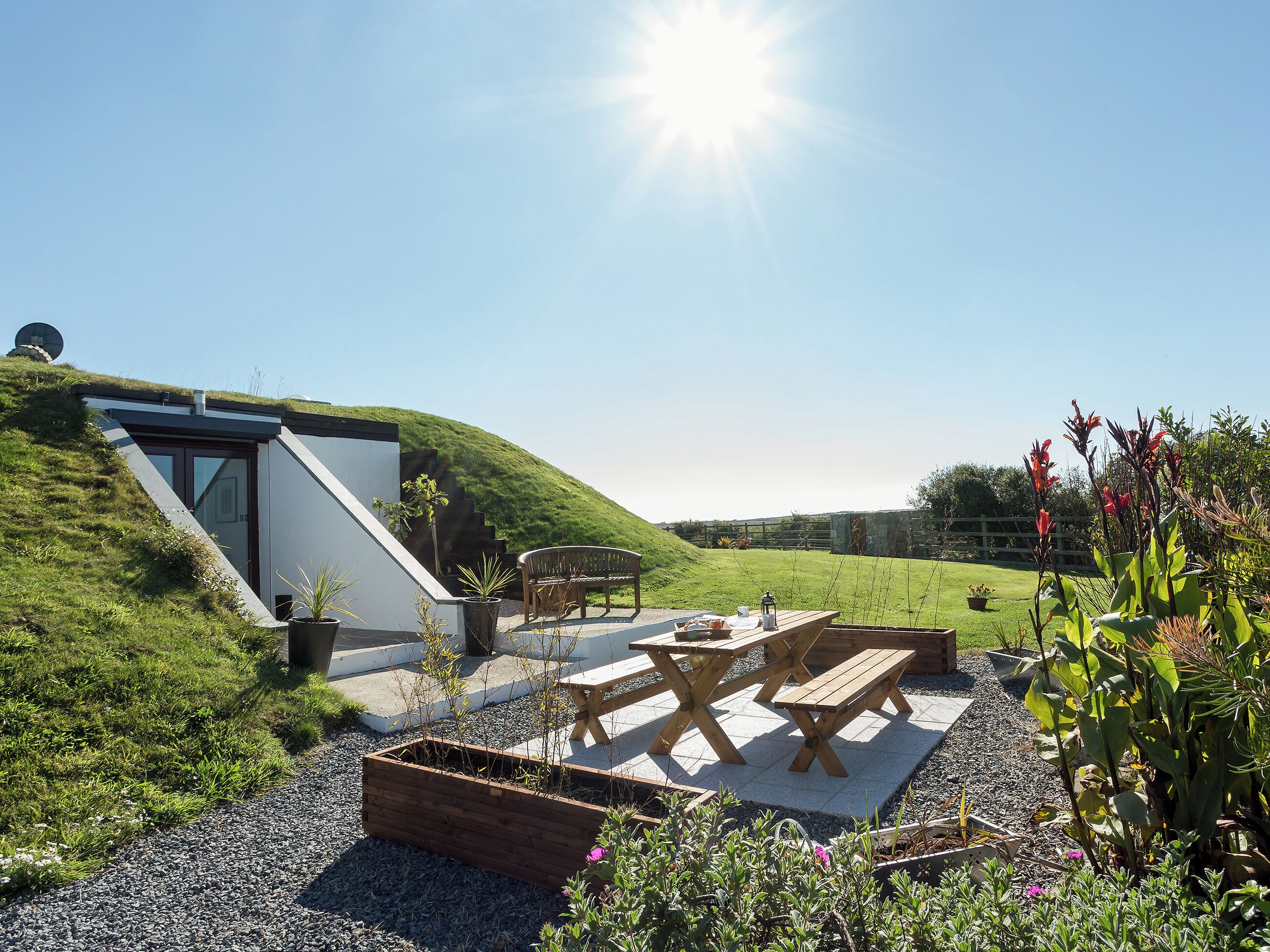 A modern house with a sloped roof, a patio with wooden furniture, and a garden.