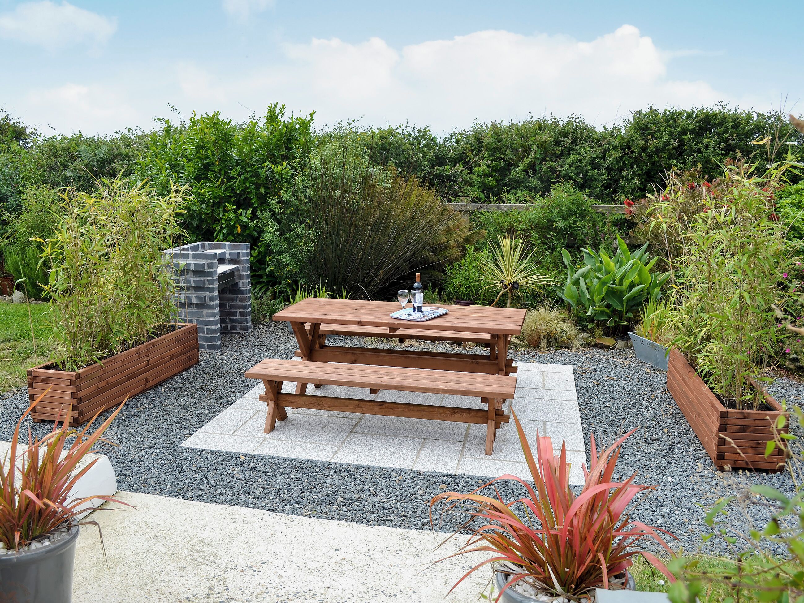 Een houten picknicktafel met bankjes, omringd door grind en potplanten.