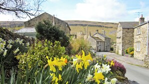 A stone building with a traditional design, a paved road, and a field in the background. - 3 bedroom accommodation in Kettlewell, near Grassington (Kettlewell, near Grassington)