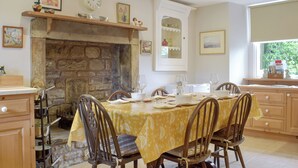 A dining area with a stone fireplace, wooden chairs, a table set for four, and a window with a view of greenery. - 3 bedroom accommodation in Kettlewell, near Grassington (Kettlewell, near Grassington)