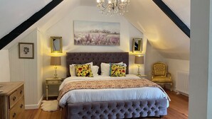 Un dormitorio con cabecera capitonada, una cama grande con ropa de cama floral, una araña y un radiador.