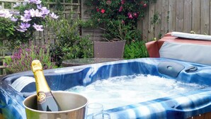 Un jacuzzi con una botella de champán y copas, rodeado de plantas y una valla de madera.