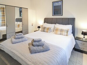 Una cama bien hecha con almohadas y toallas dobladas, una mesita de noche con lámpara, un armario y un espejo.