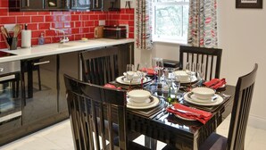 Una cocina moderna con salpicadero de baldosas rojas, armarios negros y una zona de comedor preparada para seis personas, con una mesa de vidrio, sillas y un mantel individual rojo.