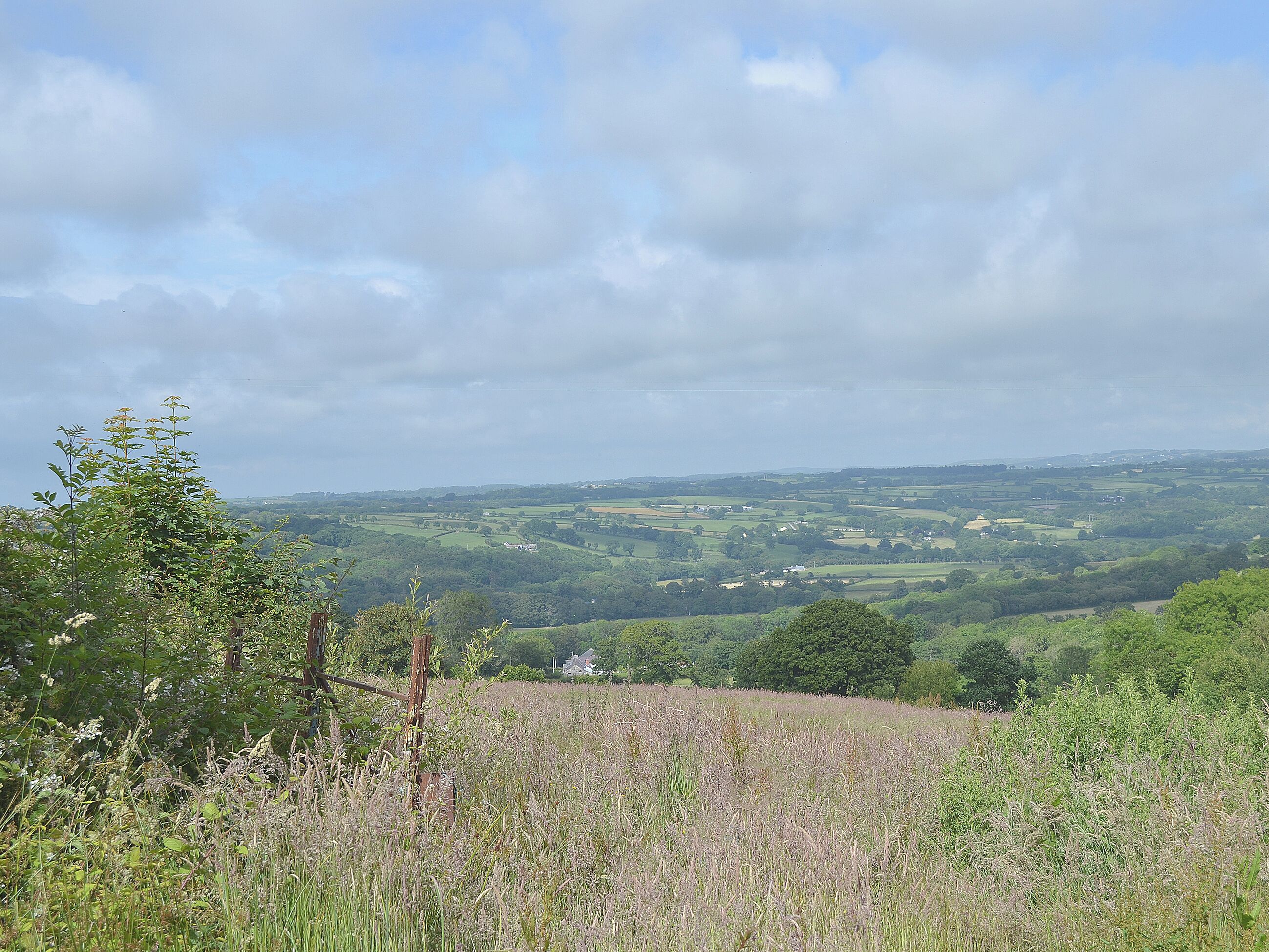 A rural landscape with rolling hills, scattered houses, and a clear sky.