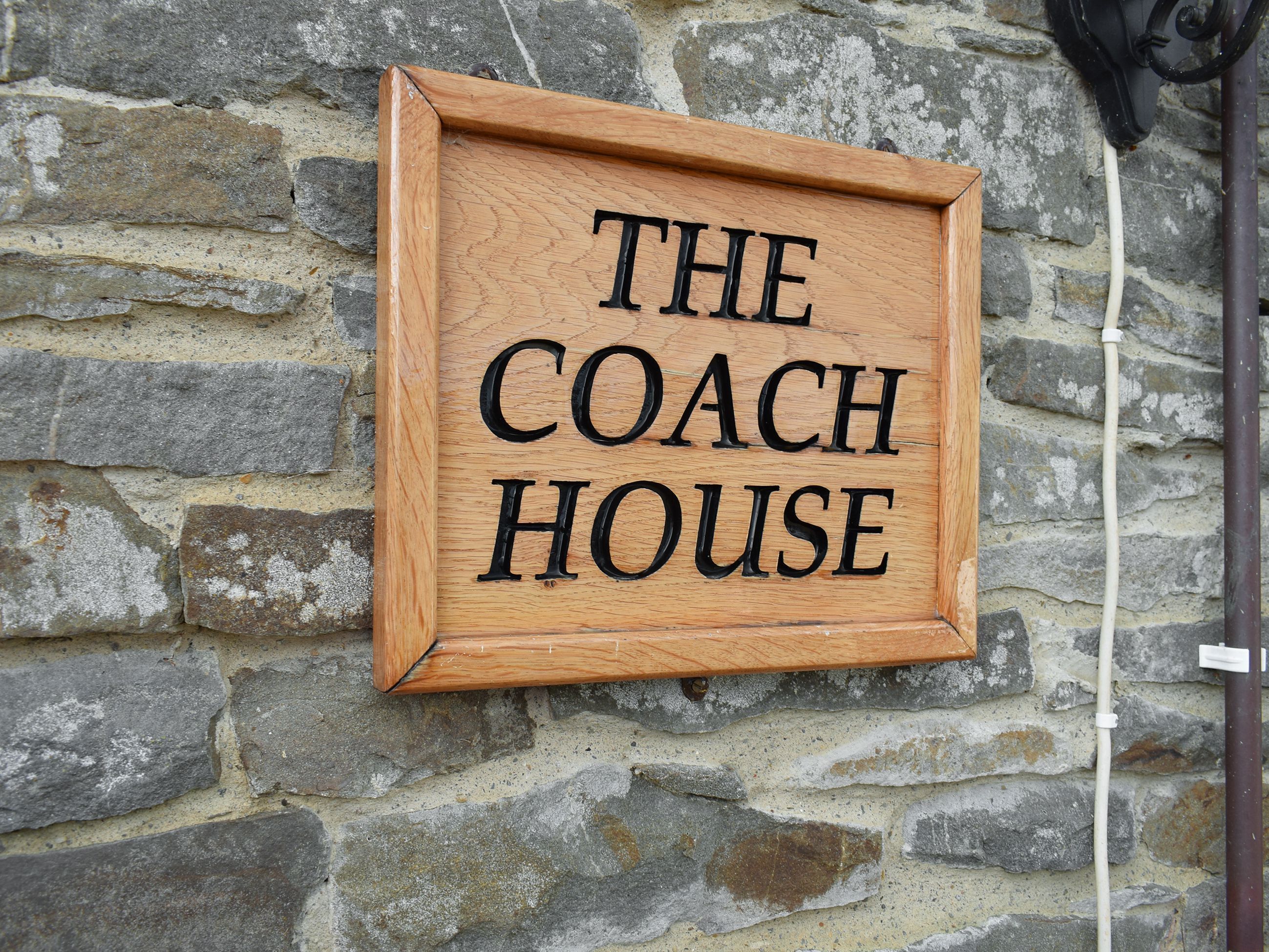Een houten bordje met de tekst 'THE COACH HOUSE' bevestigd aan een stenen muur.