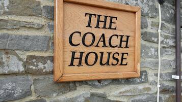 Een houten bordje met de tekst 'THE COACH HOUSE' bevestigd aan een stenen muur.