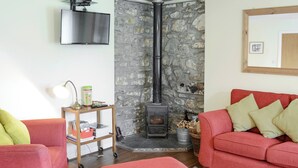 A cozy living room with a stone fireplace, a television mounted on the wall, and two red sofas with cushions. - 2 bedroom accommodation in Rosehall, near Lairg (Rosehall, near Lairg)