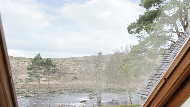 A view through a window of a natural landscape with a river, trees, and a hilly background. - 2 bedroom accommodation in Rosehall, near Lairg (Rosehall, near Lairg)