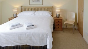 A neatly made bed with white linens and two folded towels, a wooden headboard, bedside lamps, a small wooden nightstand with drawers, and a framed picture on the wall. - 2 bedroom accommodation in Rosehall, near Lairg (Rosehall, near Lairg)