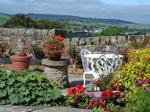 A stone wall with a white metal chair and potted plants in a garden setting.