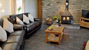 A living room with a stone wall, a fireplace, a leather sofa, a wooden coffee table, and a television. - Golygfar Mynydd - Mountain View (Pontrhydfendigaid, near Tregaron)