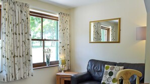 A living room with a dark leather sofa, a small wooden side table, a lamp, and a mirror on the wall.