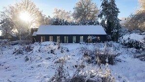 Een gebouw bedekt met sneeuw met een schuin dak, omgeven door sneeuwklare bomen en struiken.