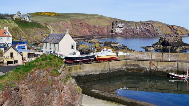 A coastal town with a harbor, boats, and a prominent white building with a steep roof.