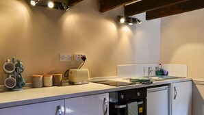 A kitchen with a white countertop, a toaster, a sink, and a dishwasher. There are cabinets below the countertop and a wooden beam above.